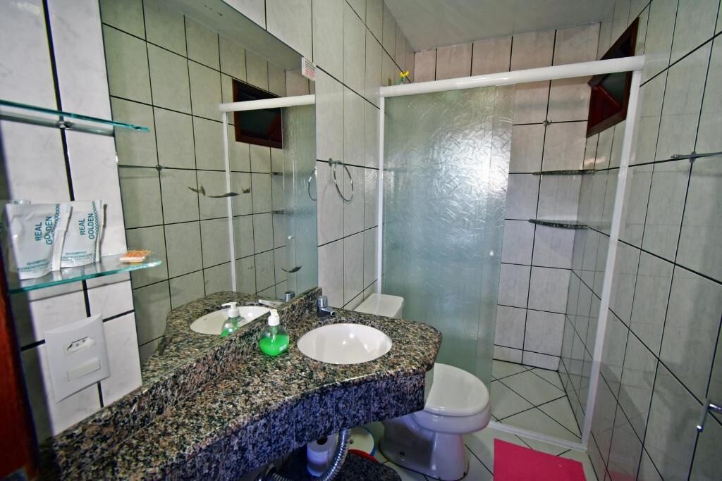 A bathroom with a granite countertop, a white sink, a glass shower enclosure, and a toilet.
