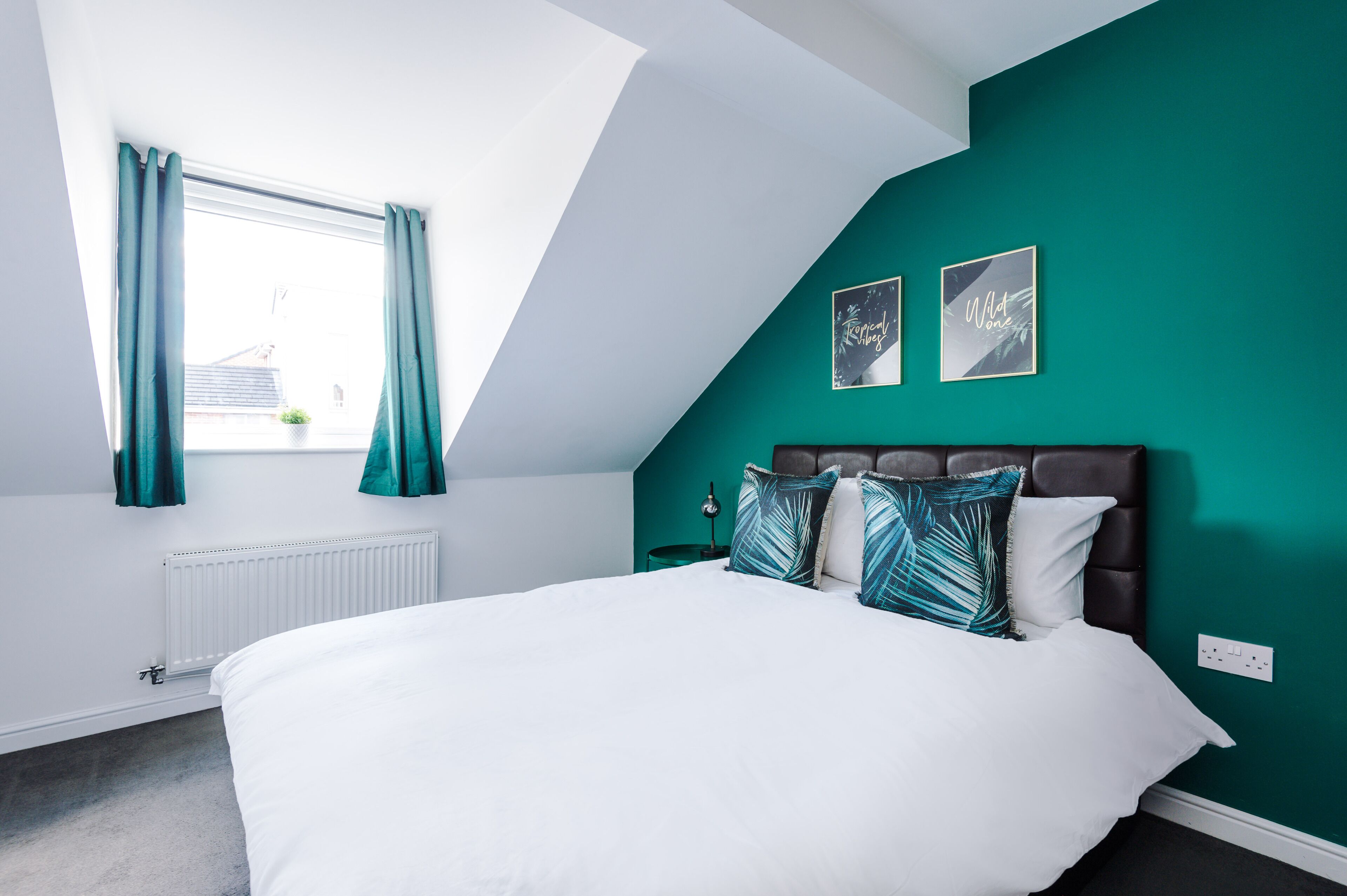 Una camera da letto con un letto bianco, pareti color acquamarina e un soffitto spiovente.