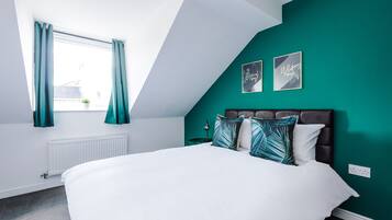Una camera da letto con un letto bianco, pareti color acquamarina e un soffitto spiovente.