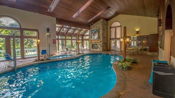 An indoor swimming pool with a stone wall, wooden ceiling, and large windows. - Nordic Village Townhouse, Storyland, Mountains, Pools (Bartlett)