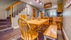A dining area with a wooden table and chairs, a bench, and a staircase with a wooden railing. - Nordic Village Townhouse, Storyland, Mountains, Pools (Bartlett)