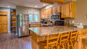 A kitchen with wooden cabinets, a granite countertop, a stainless steel refrigerator, and a built-in oven. - Nordic Village Townhouse, Storyland, Mountains, Pools (Bartlett)