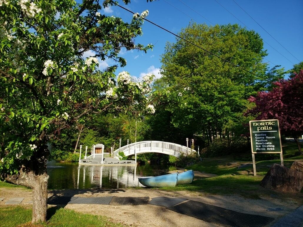 Un parque con un puente, barcos y un cartel que indica Cascada Nórdica, con servicios como una sala de fogata, un pabellón, botes, patinaje sobre hielo y área de picnic.