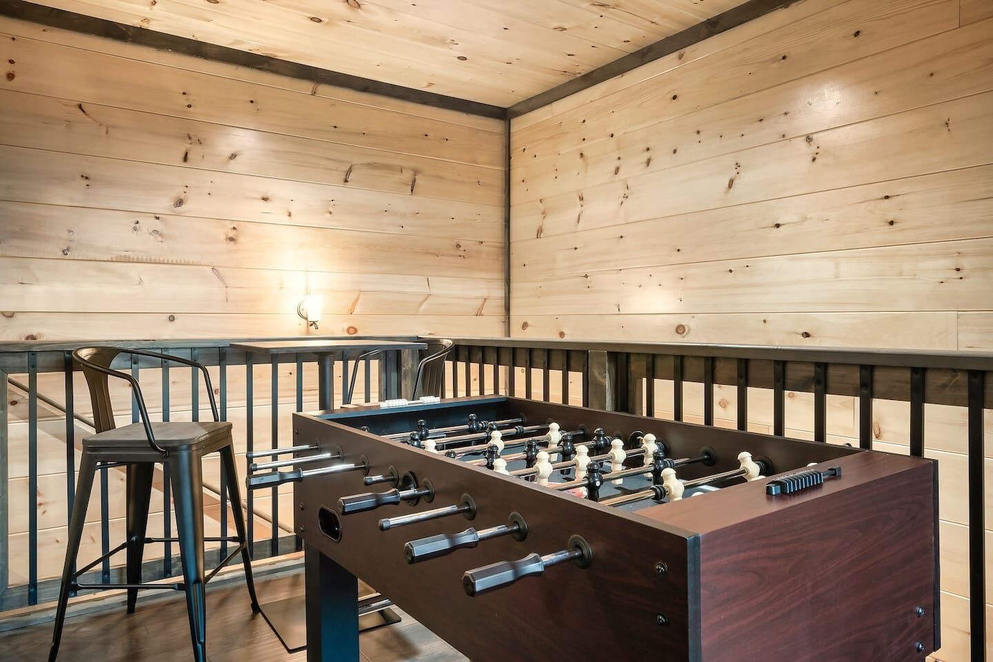 Une pièce au plancher de bois, équipée d’un baby-foot et de deux tabourets de bar.