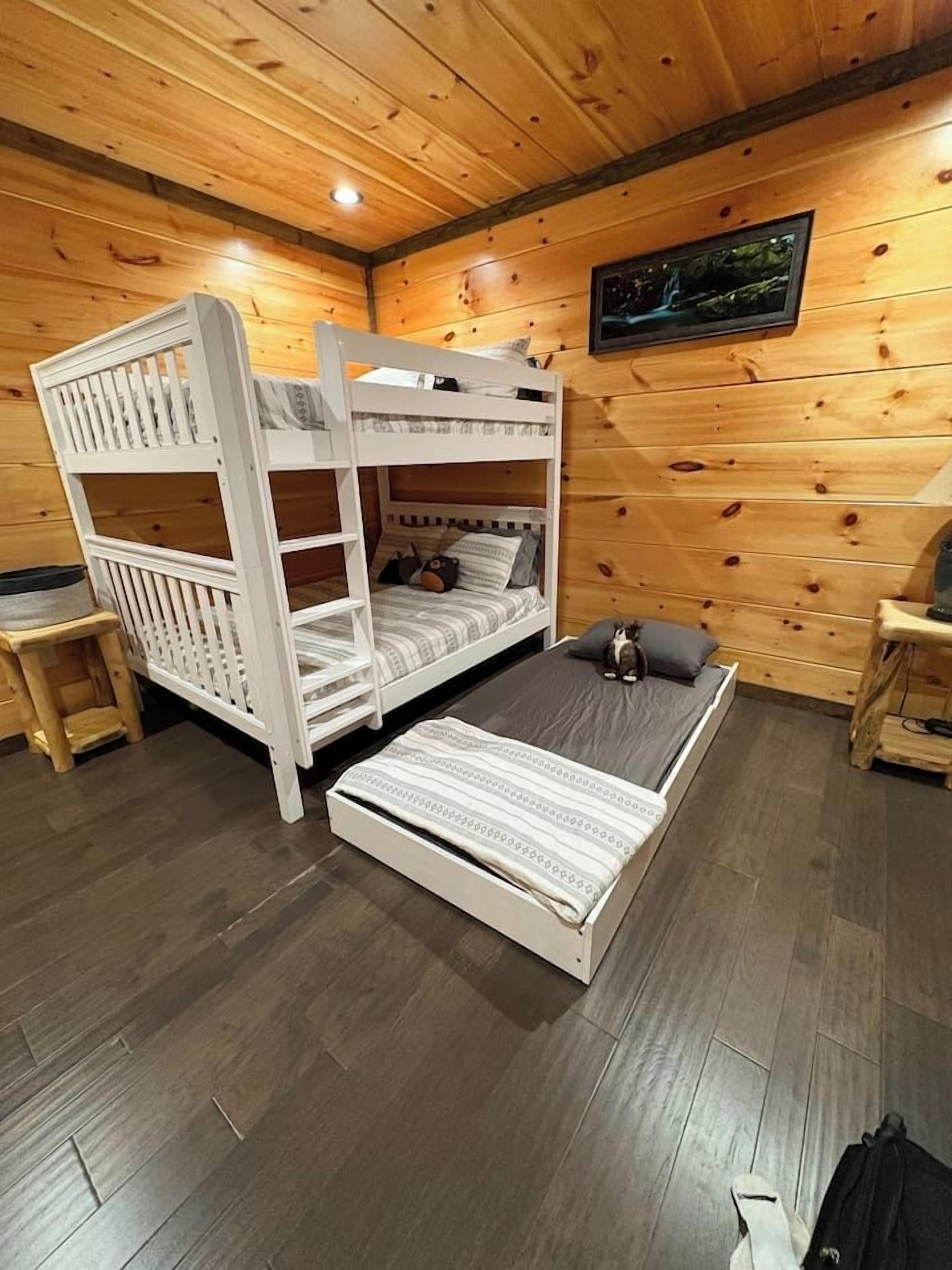 Habitació amb lliteres, sòl i parets de fusta, una taula petita i un quadre a la paret.