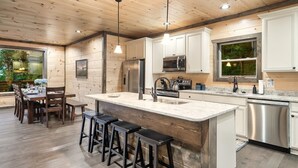 A modern kitchen with wooden ceiling, stainless steel appliances, and a large island with bar stools. - Private Indoor Heated Pool, Mtn Views, Hot Tub, Fire Pit, Location, Fast Wifi (Sevierville)