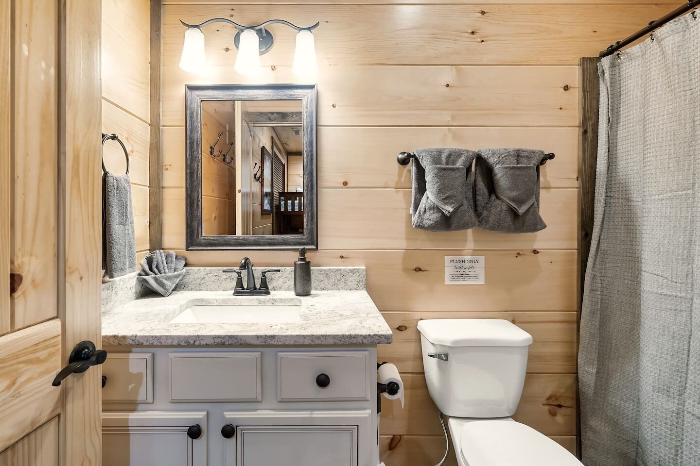 Un baño con detalles de madera, un lavamanos con espejo, un inodoro y una cortina de ducha.