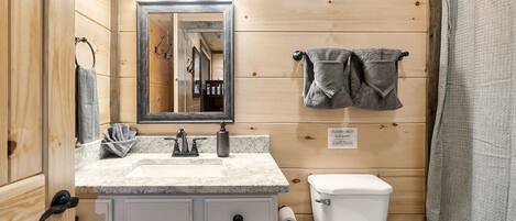 Un baño con detalles de madera, un lavamanos con espejo, un inodoro y una cortina de ducha.