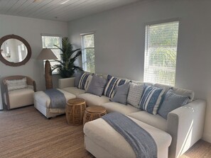 A living room with a beige sectional sofa, striped pillows, a round wooden coffee table, a woven floor rug, a round mirror, and a tall floor lamp.