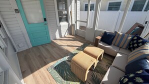 Una habitación soleada con una puerta azul verdosa, piso de madera, sofá con cojines estampados y una cesta tejida.