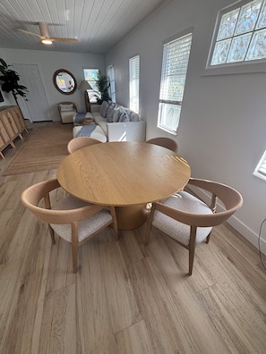 A dining area with a round wooden table and wicker chairs, a sofa, and a ceiling fan.