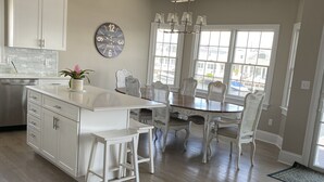Une cuisine spacieuse avec des meubles blancs, un îlot central doté de tabourets et un coin repas avec des chaises blanches.