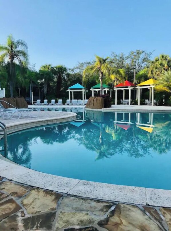 Ein Swimmingpool mit Liegestühlen und Gazebos, umgeben von Palmen.