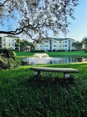 A park with a fountain, a bench, and a building in the background.