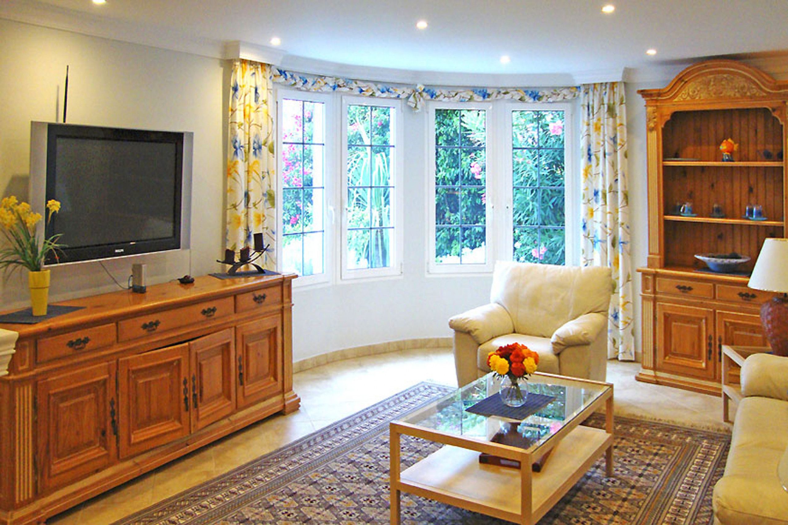 A living room with a television, a sofa, a coffee table with flowers, and a wooden cabinet.