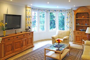 A living room with a television, a sofa, a coffee table with flowers, and a wooden cabinet.