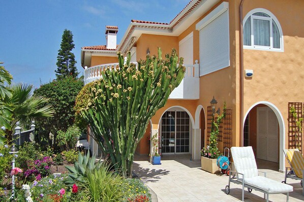 A Mediterranean-style building with a garden, outdoor seating, and a large cactus.