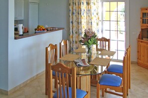 A dining area with a glass table surrounded by wooden chairs with blue cushions, a vase with flowers, and a fruit basket on the counter. - Apartamento Laguna with shared swimming pool (Chayofa)
