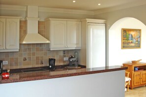 A kitchen with white cabinets, a granite countertop, a coffee maker, and a painting on the wall.