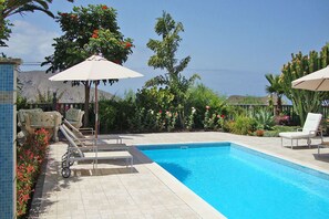 A swimming pool with lounge chairs and umbrellas, surrounded by greenery and flowers.