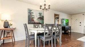 A dining area with a round table, six chairs, a chandelier, a painting, a television, and a lamp. - Short Walk to Downtown, AC, Coffee Bar, Patio (Enumclaw)