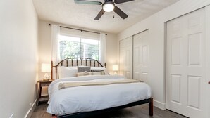 A bedroom with a bed, bedside tables, a ceiling fan, and a window with blinds. - Short Walk to Downtown, AC, Coffee Bar, Patio (Enumclaw)