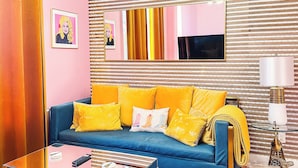 A modern living room with a blue sofa, yellow cushions, a glass coffee table, and a patterned wall.