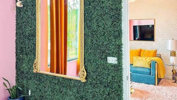 A room with a green wall, a large mirror, a pink wall, a blue sofa, and a pink rug.