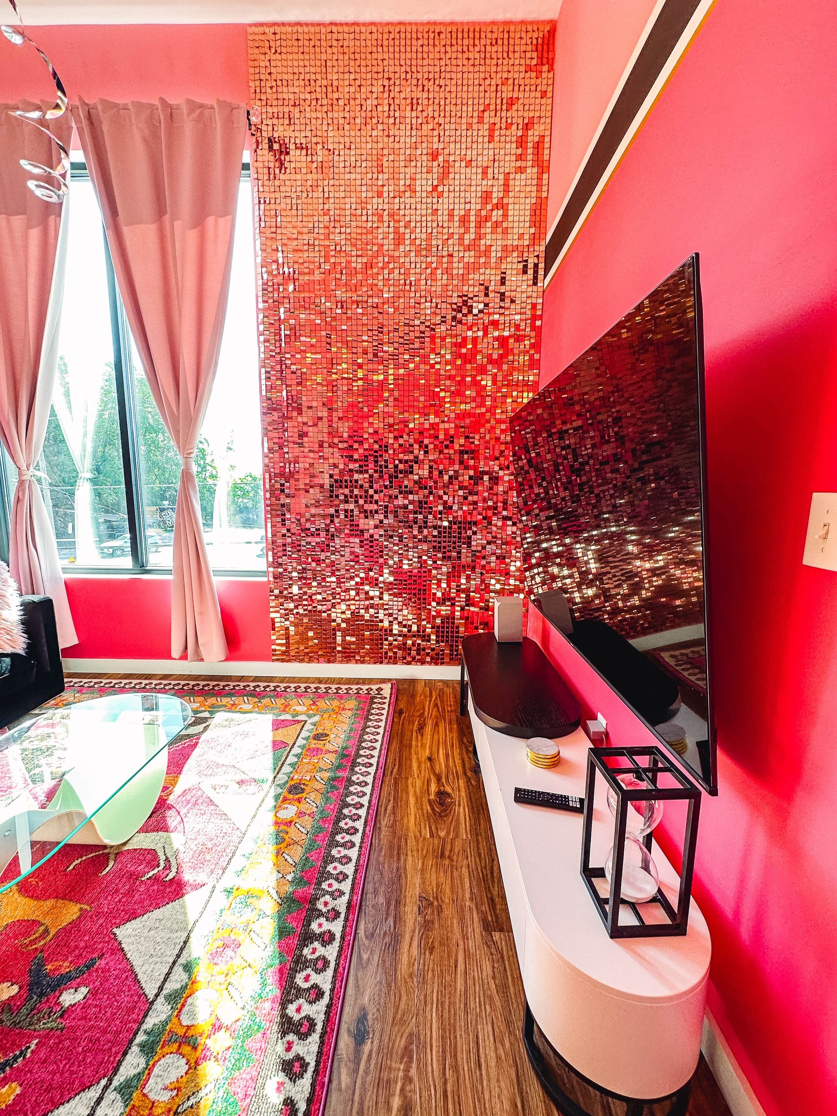 A modern living room with a large TV, a patterned rug, and a red wall with a mosaic design.