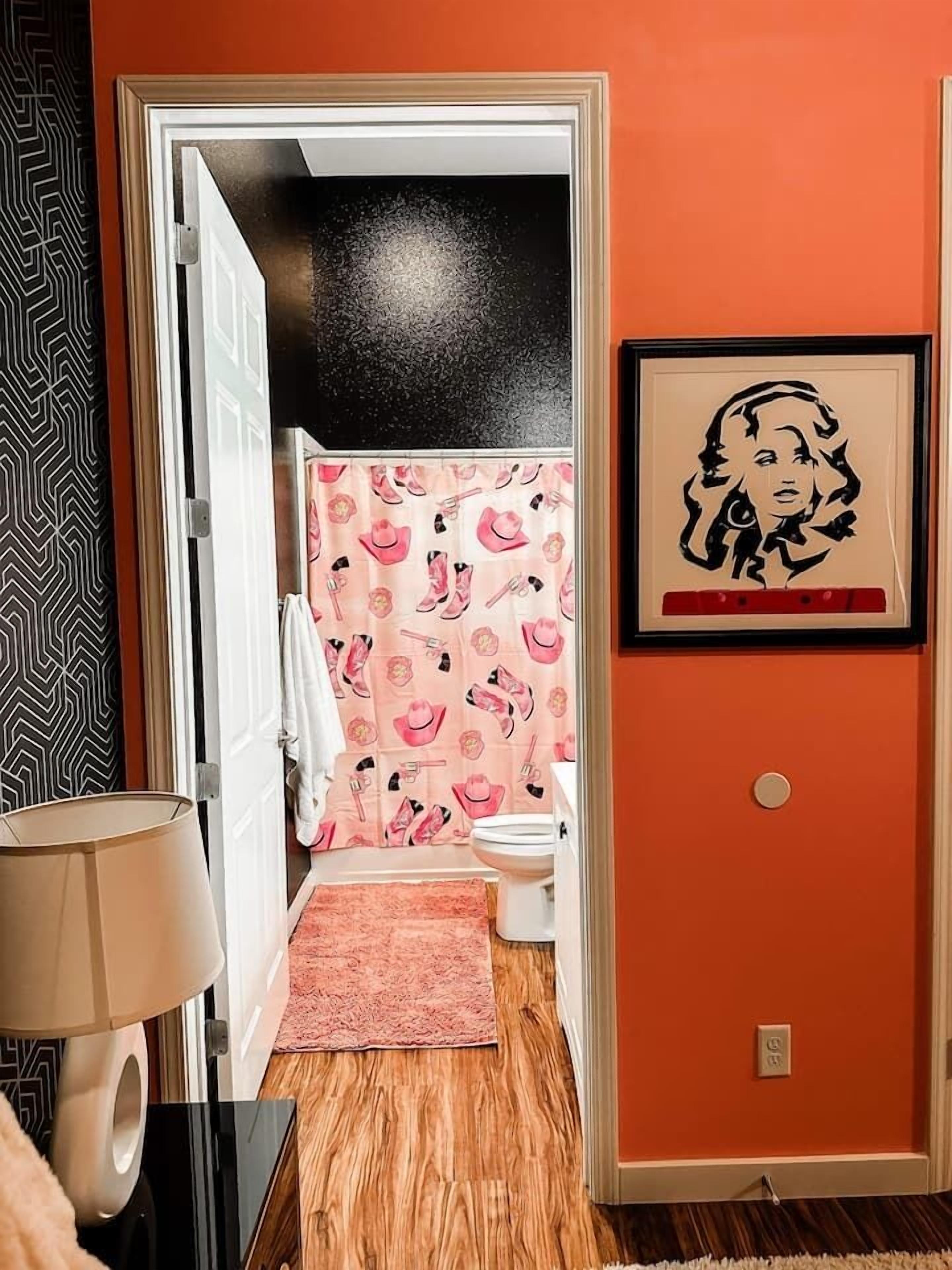 Een badkamer met douchegordijn met een roze en zwart patroon, een wit toilet en een roze vloerkleed.