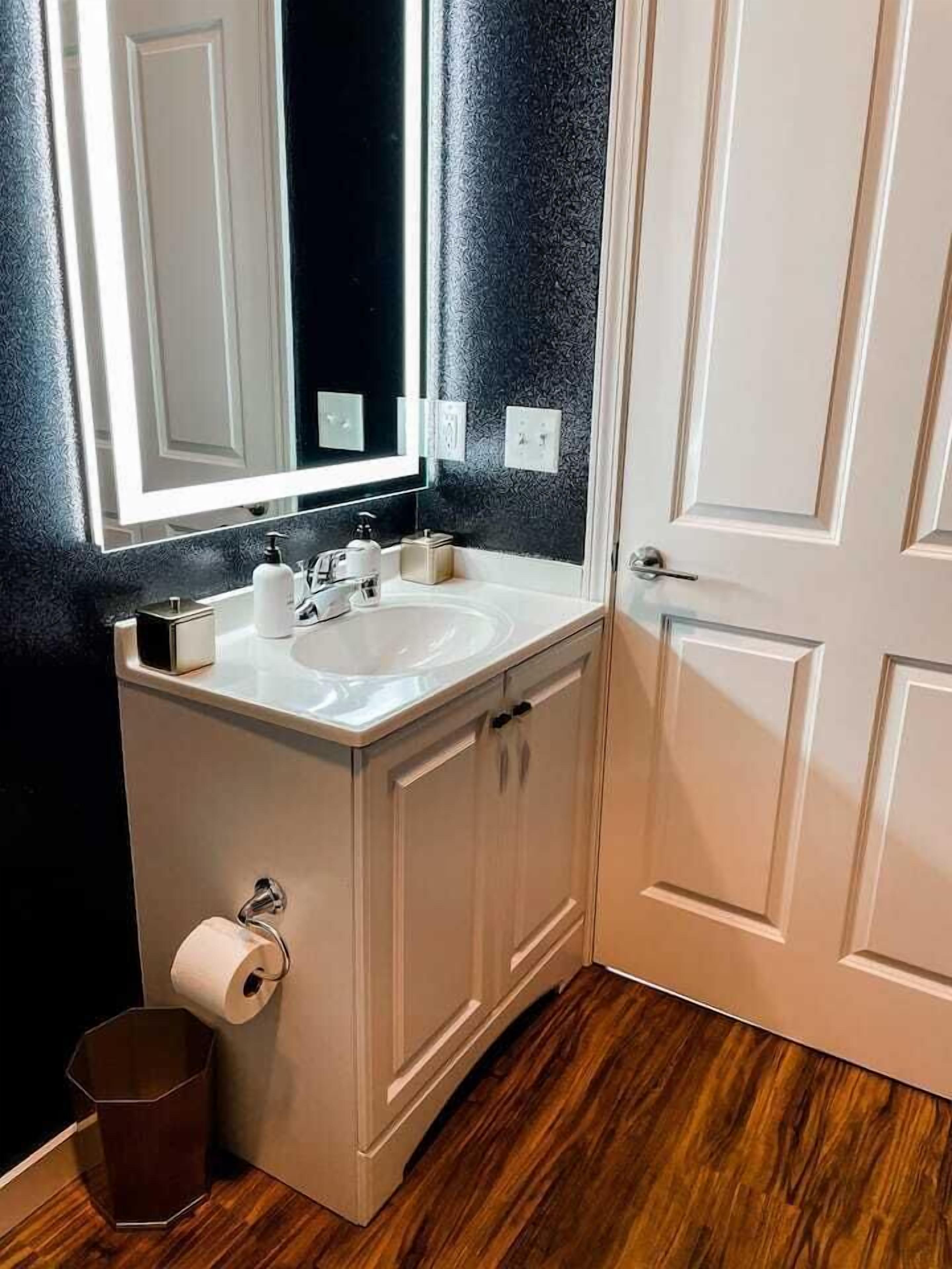 Un baño con lavamanos blanco, un espejo y un dispensador de papel higiénico.