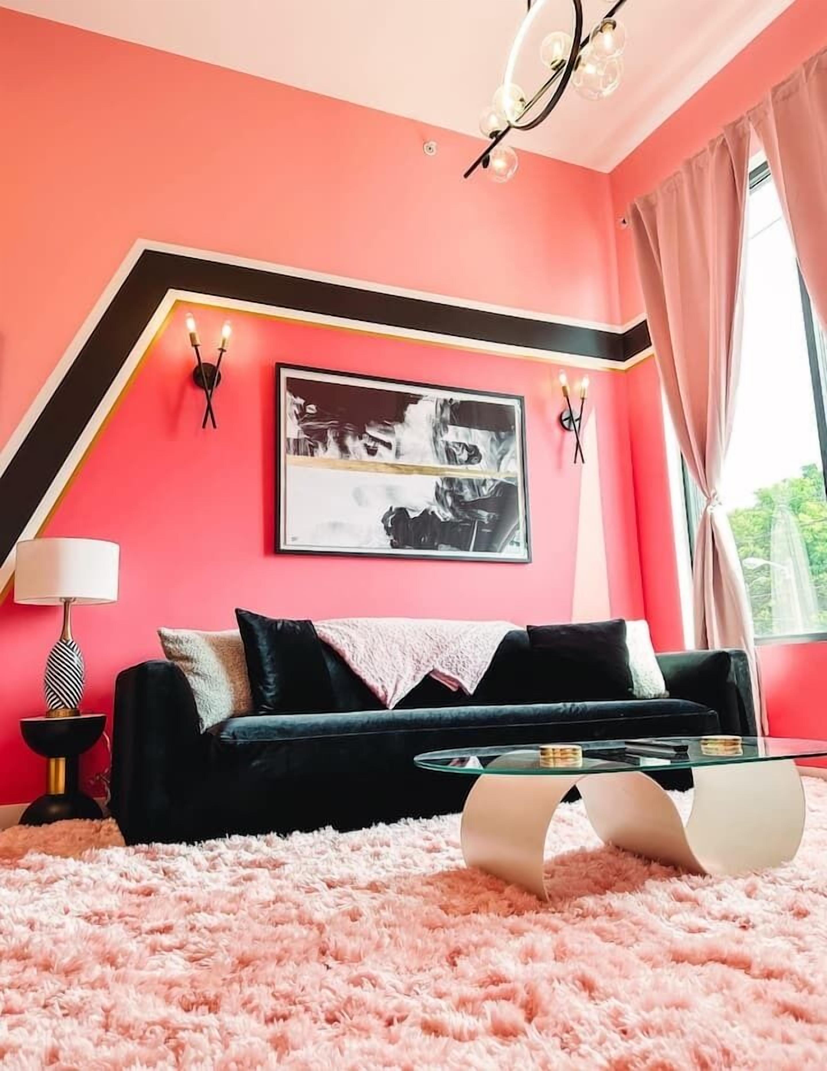 A modern living room with a black sofa, a glass coffee table, and a pink shag rug.