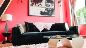 Un salon moderne avec un canapé noir, une table basse en verre et un tapis à longues mèches rose.