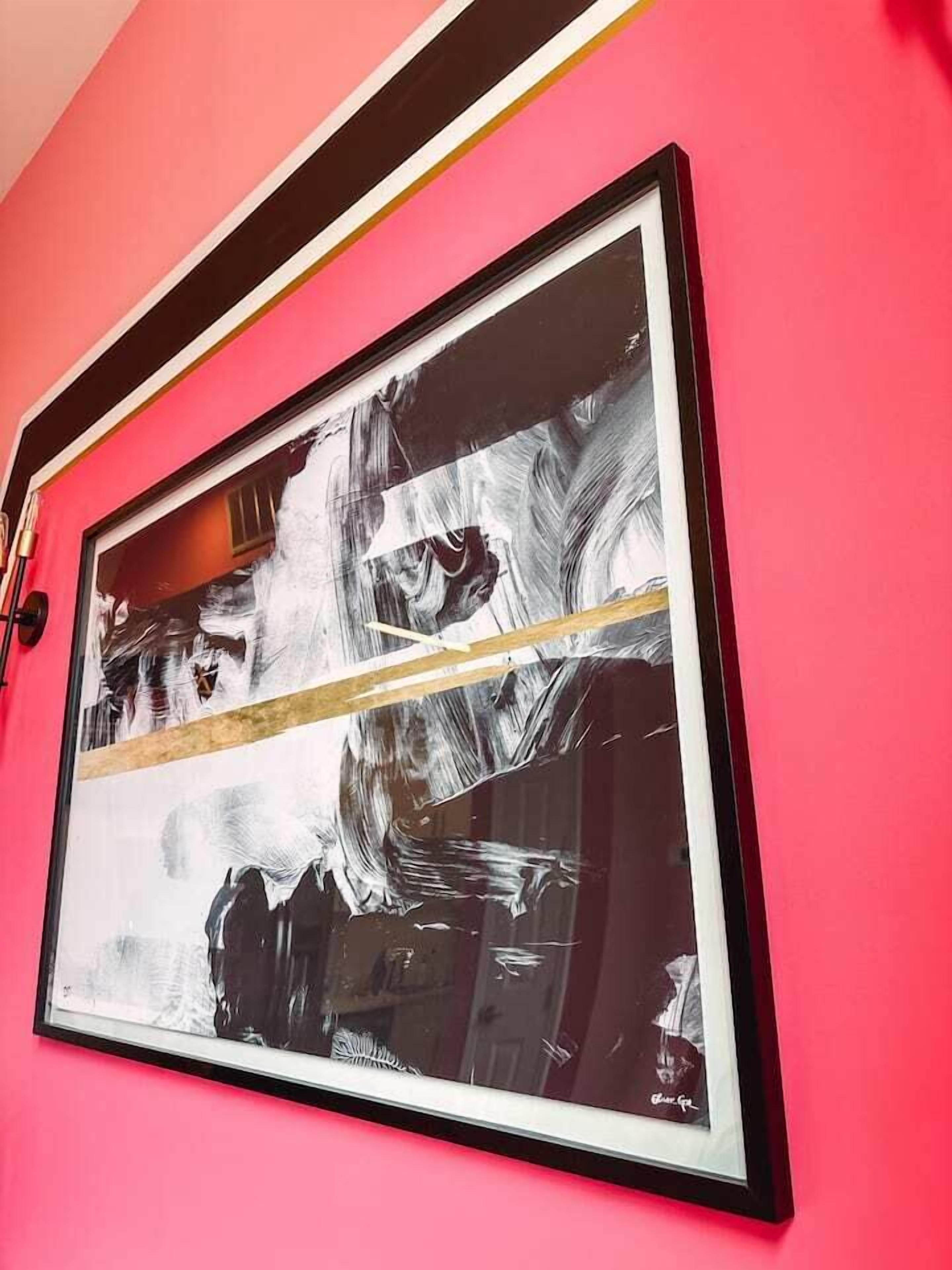 A framed abstract painting on a pink wall.