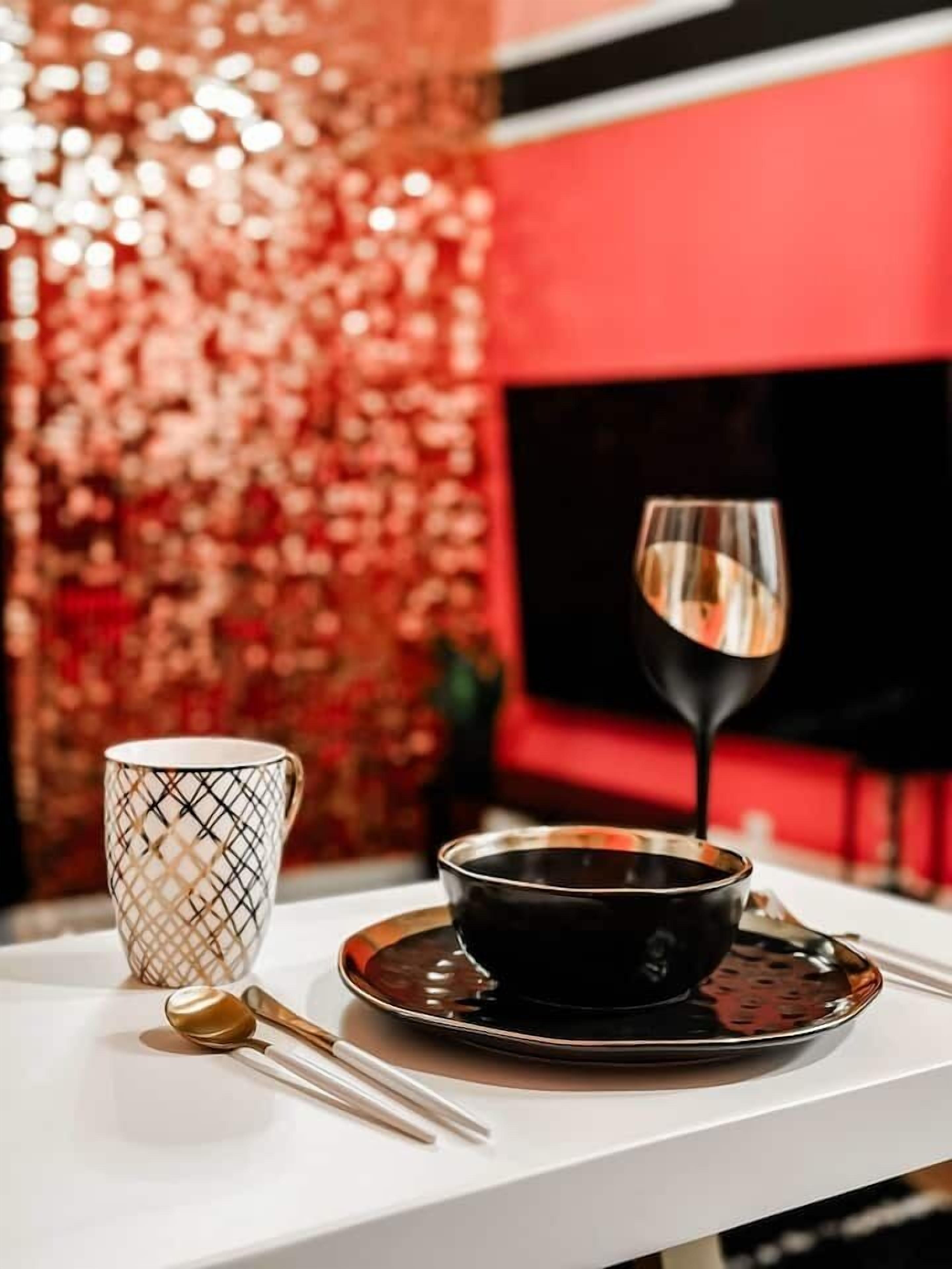 A table with a black bowl, a white mug, and a gold spoon on a white surface.