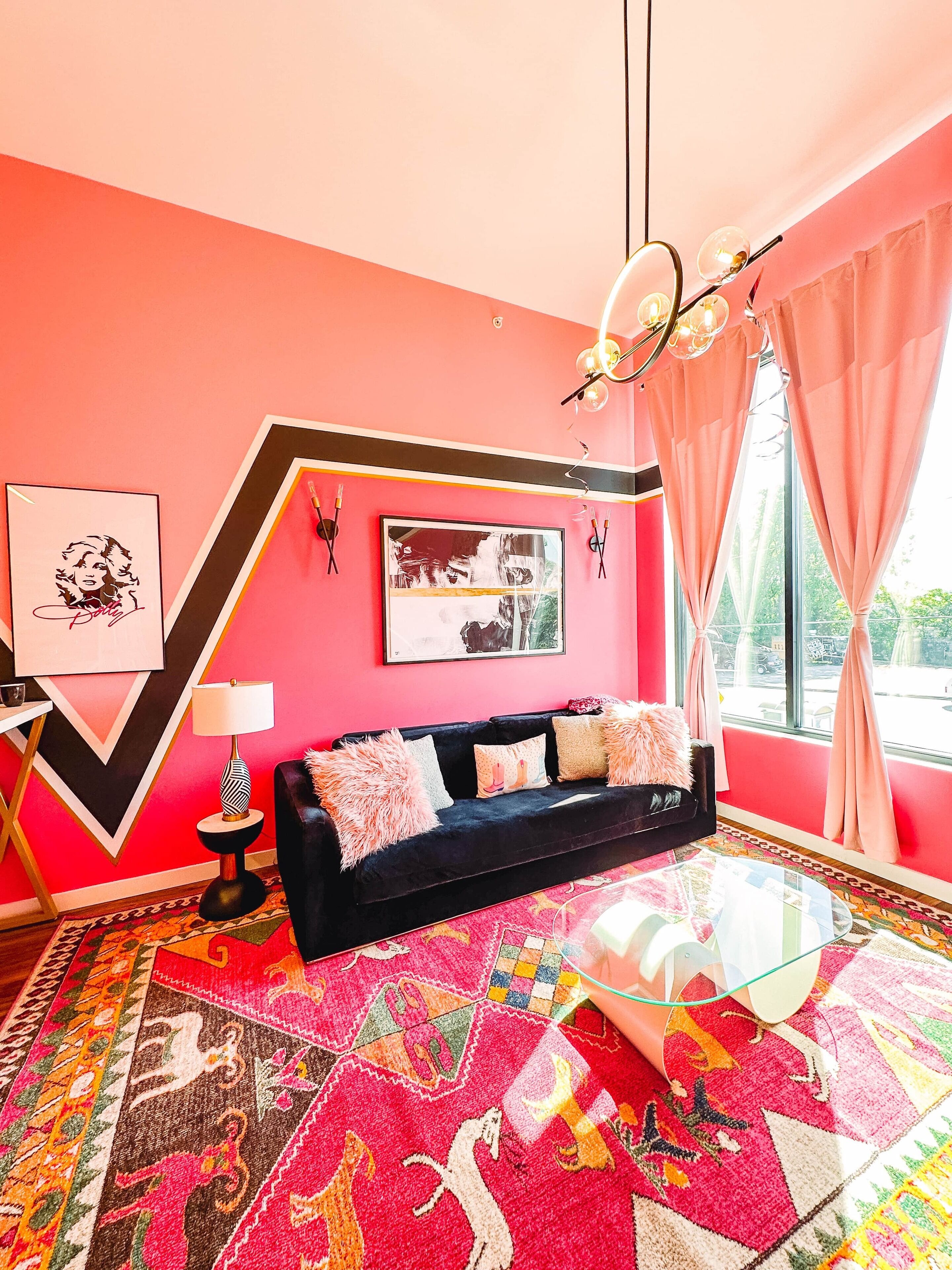 A vibrant room with a black sofa, colorful rugs, and a large window with curtains.