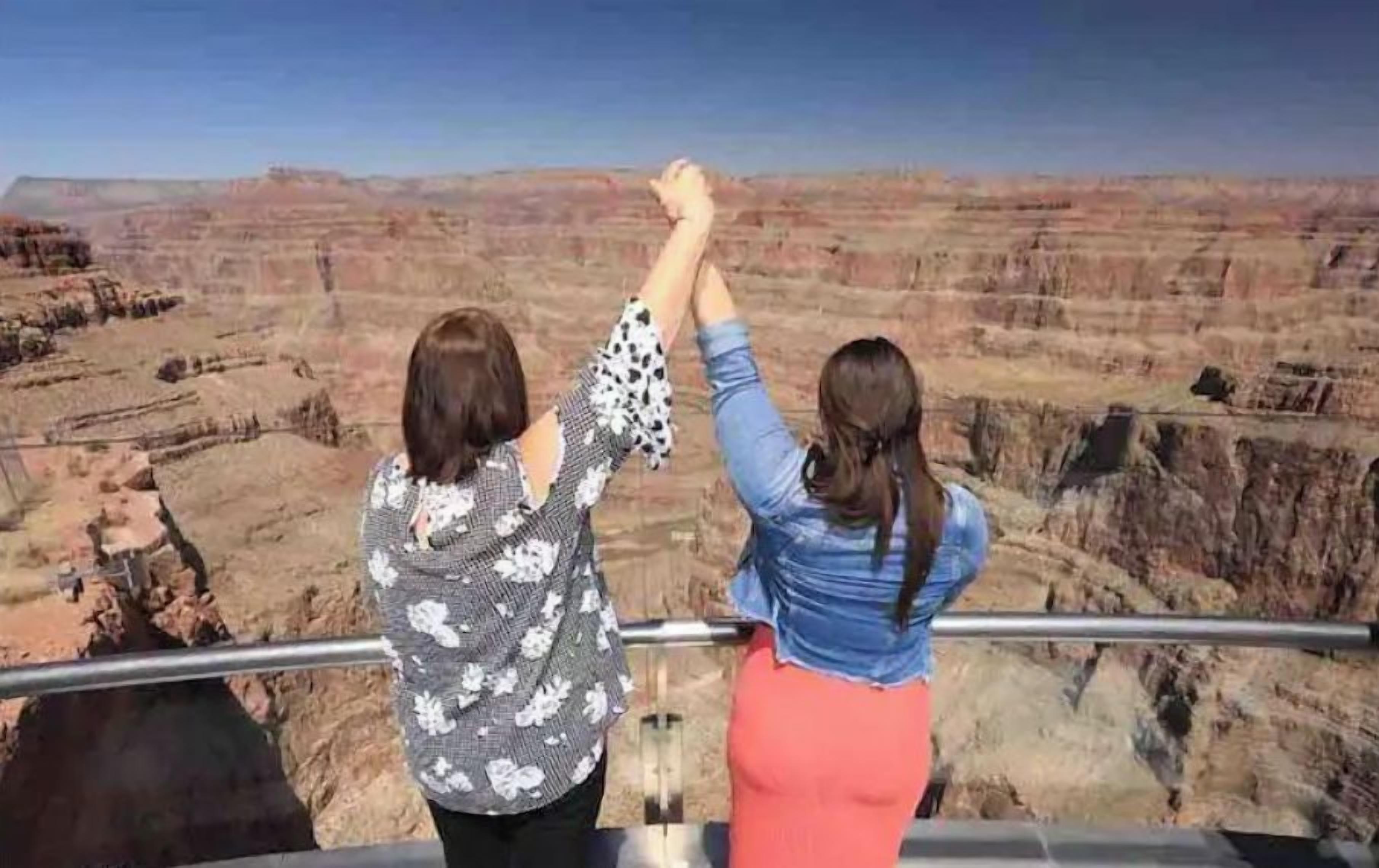 Twee personen houden elkaars hand vast op een balkon met uitzicht op de Grand Canyon.