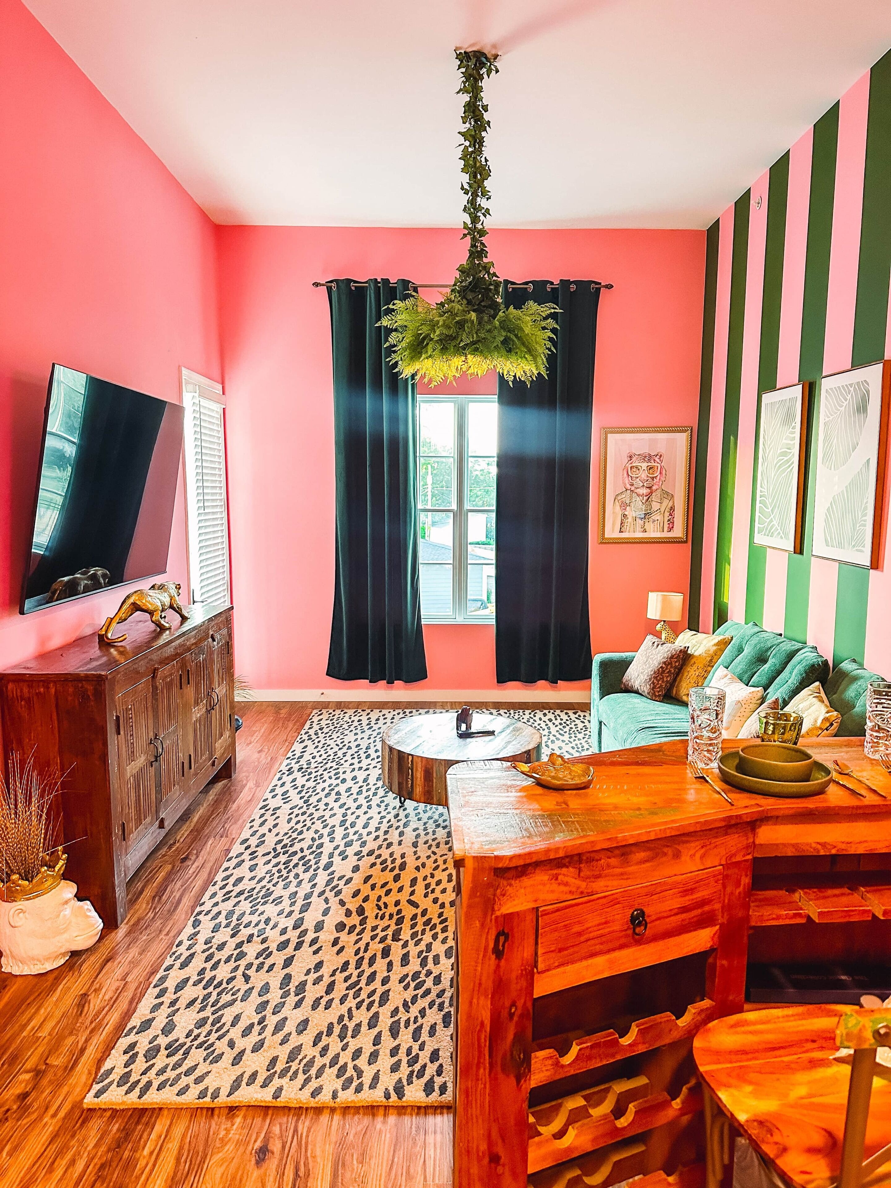 Un salon avec un mur rose, une table basse en bois, un canapé, un téléviseur et une fenêtre avec des rideaux.