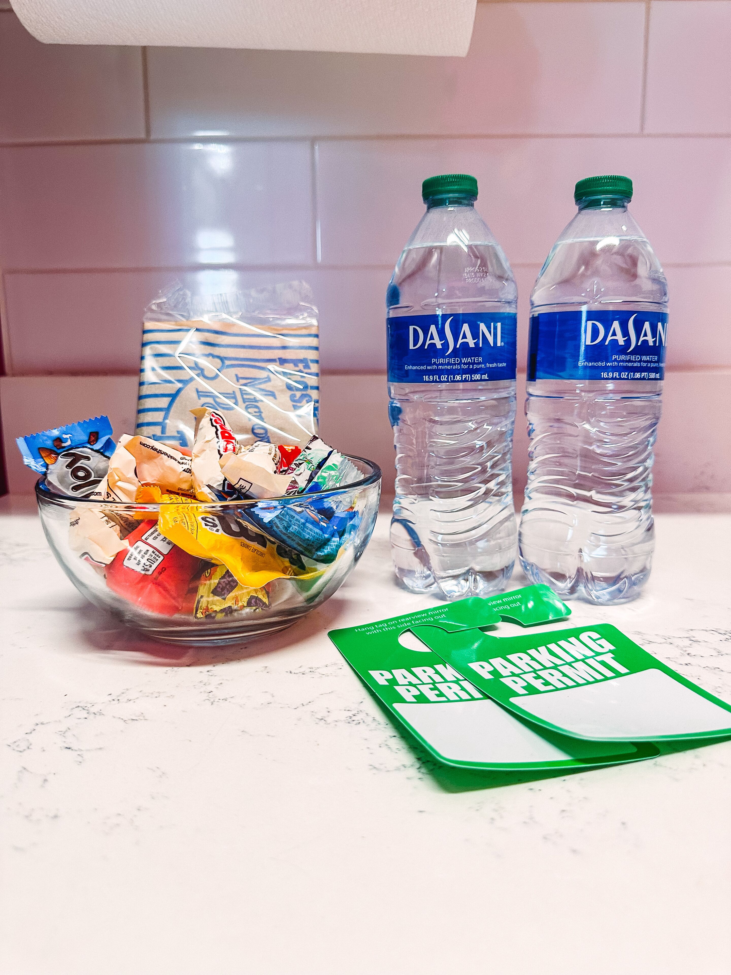 A bowl of snacks, two Dasani water bottles, and a green parking permit on a marble countertop.