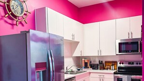 Uma cozinha moderna com armários brancos, eletrodomésticos de aço inoxidável e uma parede com detalhes em rosa.