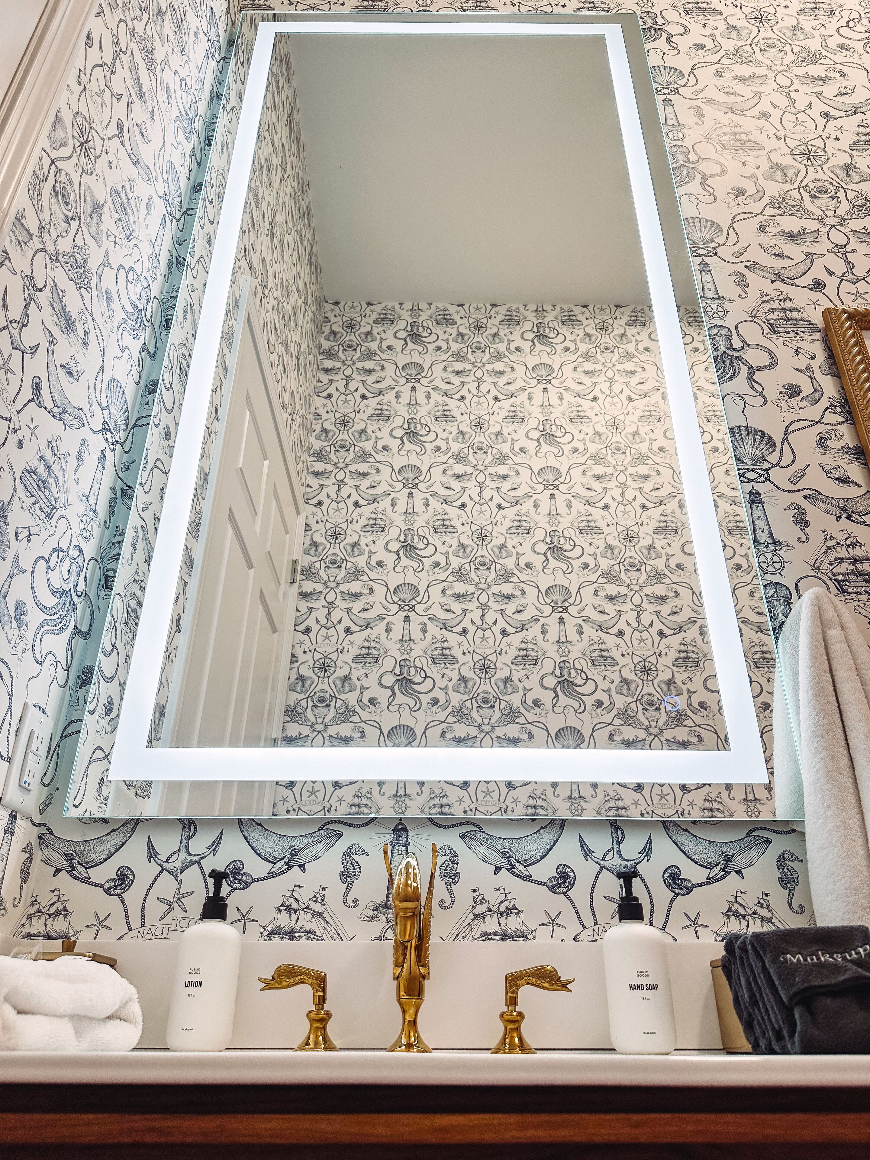 A bathroom with a mirror, nautical-themed wallpaper, and a vanity with toiletries.