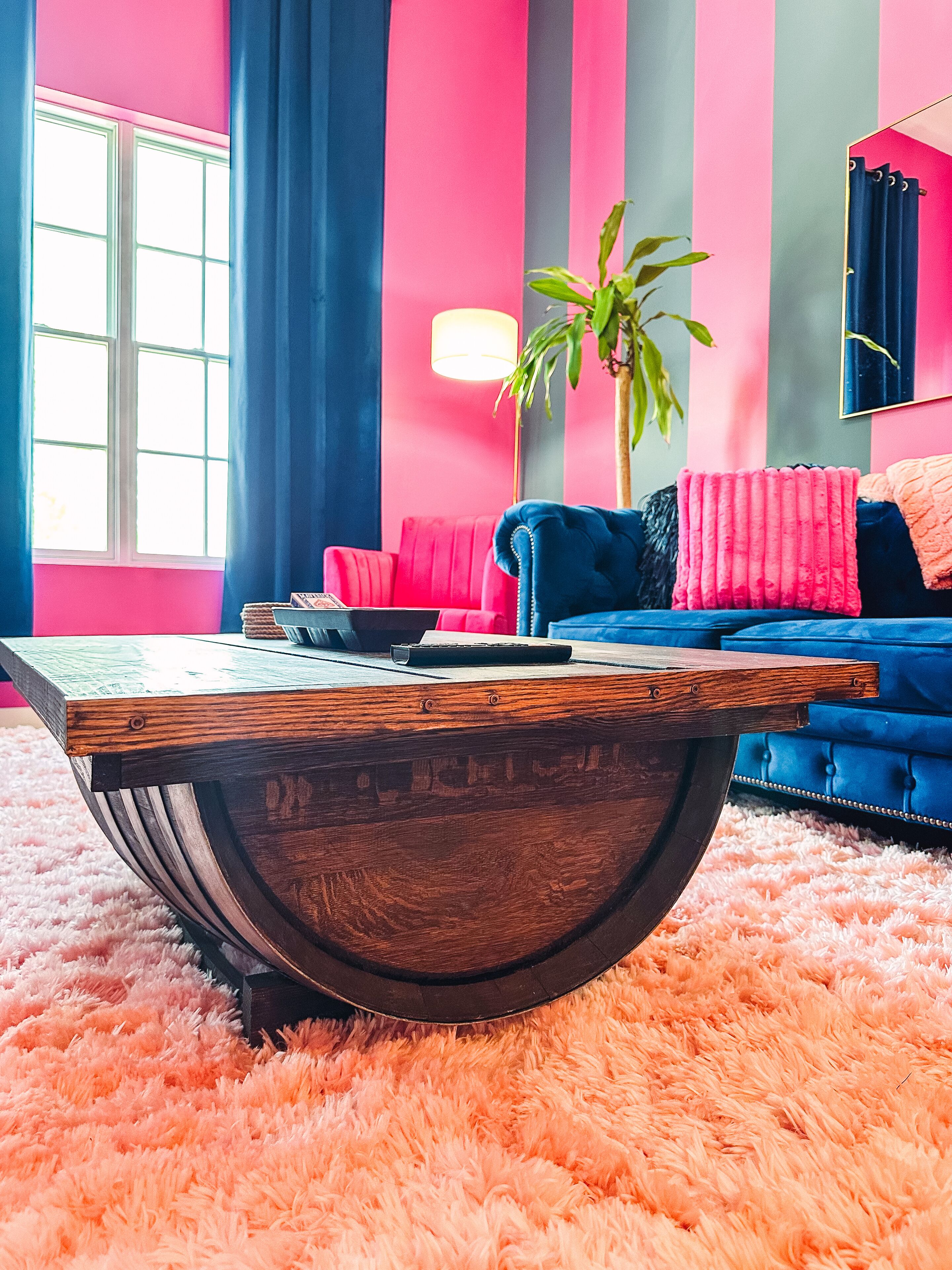 A modern living room with a round wooden coffee table, a blue sofa, and a pink rug.