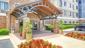 A hotel entrance with a covered walkway, stone facade, and a parking area. - Equipped Studio | Top Location, Gym Access + Pool (Gulf Shores)