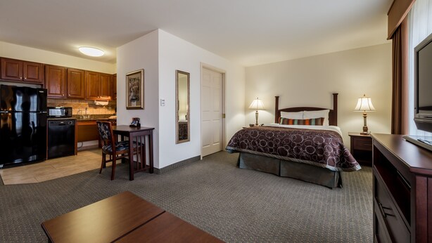 A hotel room with a bed, bedside tables, a desk, a chair, a kitchenette, and a TV. - Equipped Studio | Top Location, Gym Access + Pool (Gulf Shores)
