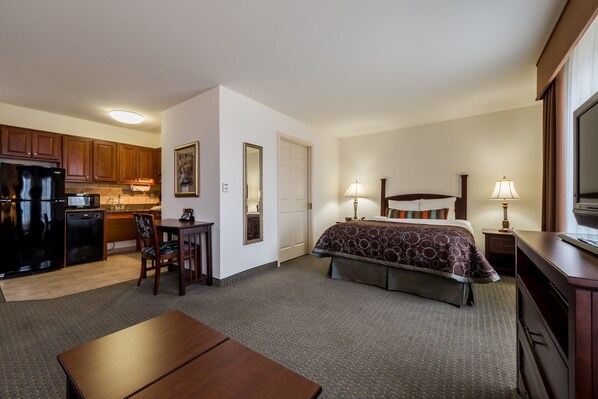 A hotel room with a bed, bedside tables, a desk, a chair, a kitchenette, and a TV. - Equipped Studio | Top Location, Gym Access + Pool (Gulf Shores)