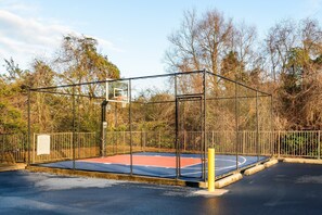 An outdoor basketball court enclosed by a metal fence, surrounded by trees and a clear sky. - Equipped Studio | Top Location, Gym Access + Pool (Gulf Shores)