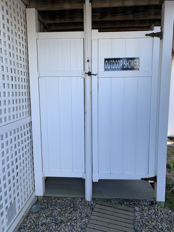 Una verja blanca con un cartel que dice 'OUTDOOR SHOWER' y una terraza de madera que la conduce.
