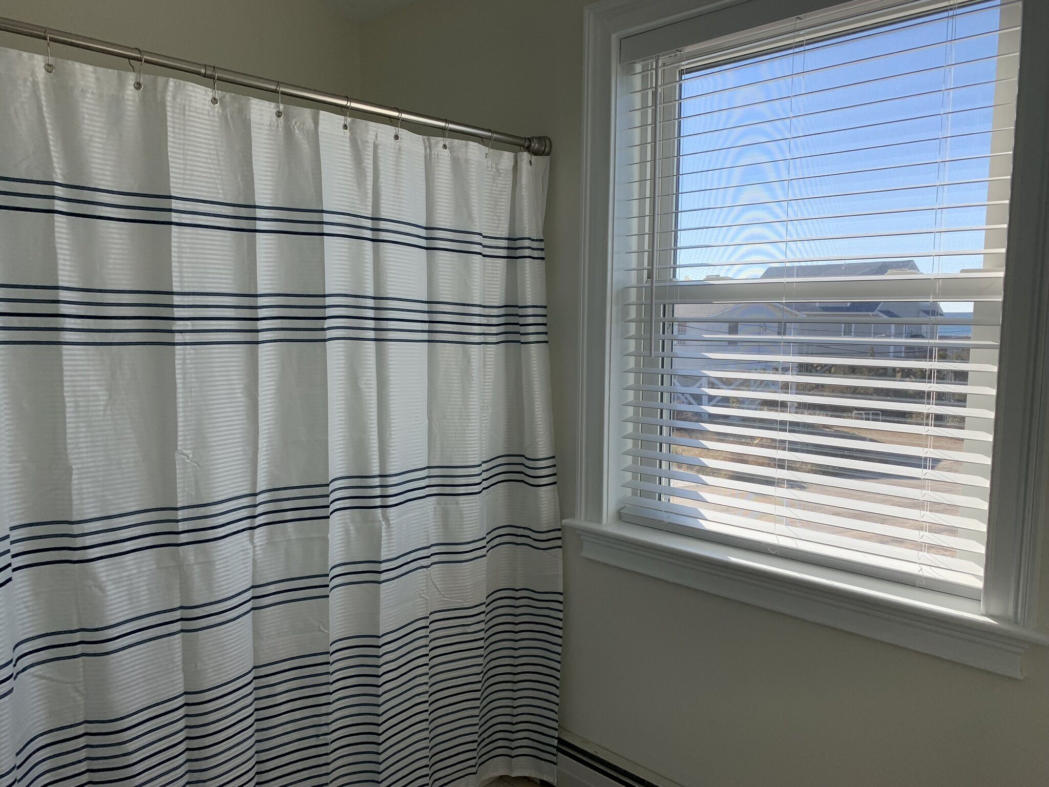 Ein Badezimmer mit einem gestreiften Duschvorhang, einem Fenster mit Jalousien und Blick auf ein Gebäude.