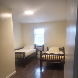 Two beds with matching headboards and footboards, a window with blinds, and air conditioning unit.