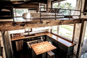 A loft-style bedroom with a bunk bed, a wooden dining table, and a kitchen area with a sink and stove. - Gorgeous Tiny House, Peaceful Hills, Amazing Views (Ponca)